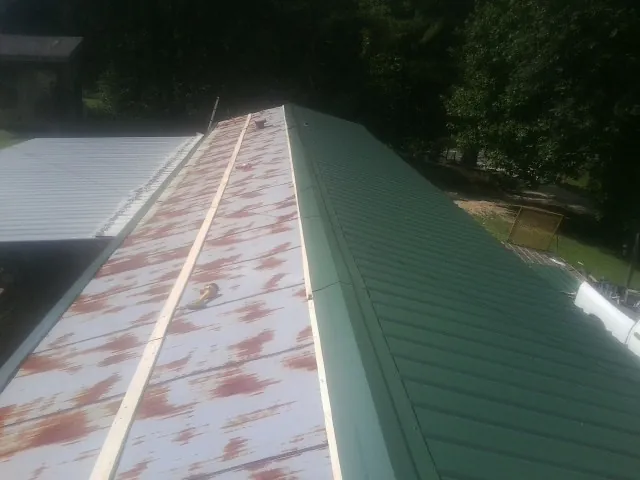 Old rusted panels beside newly installed green metal roofing — Wind Damage Roof Repair by Roofing Brothers in Warwick