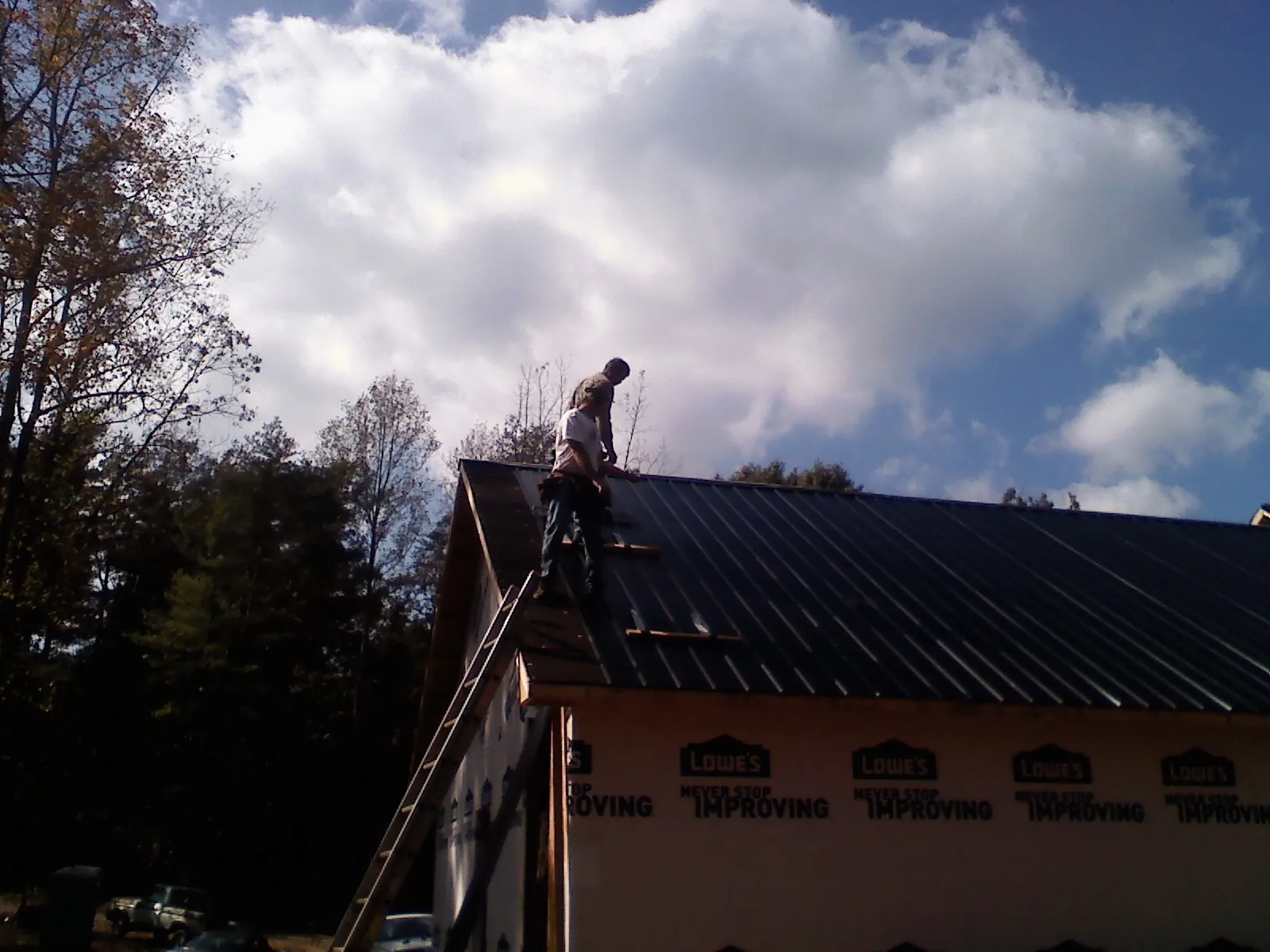 Roofer fastening dark metal panels high against a cloudy sky, from a Roof Inspection job in Warwick